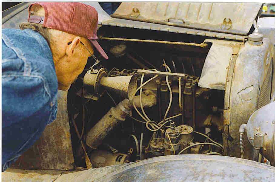 An old-timer peers into the engine compartment of a vintage automobile at the swap meet